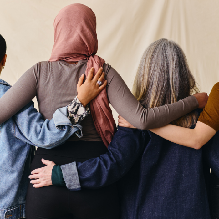 Photo of a group of women with their backs to the camera with their arms around eachother