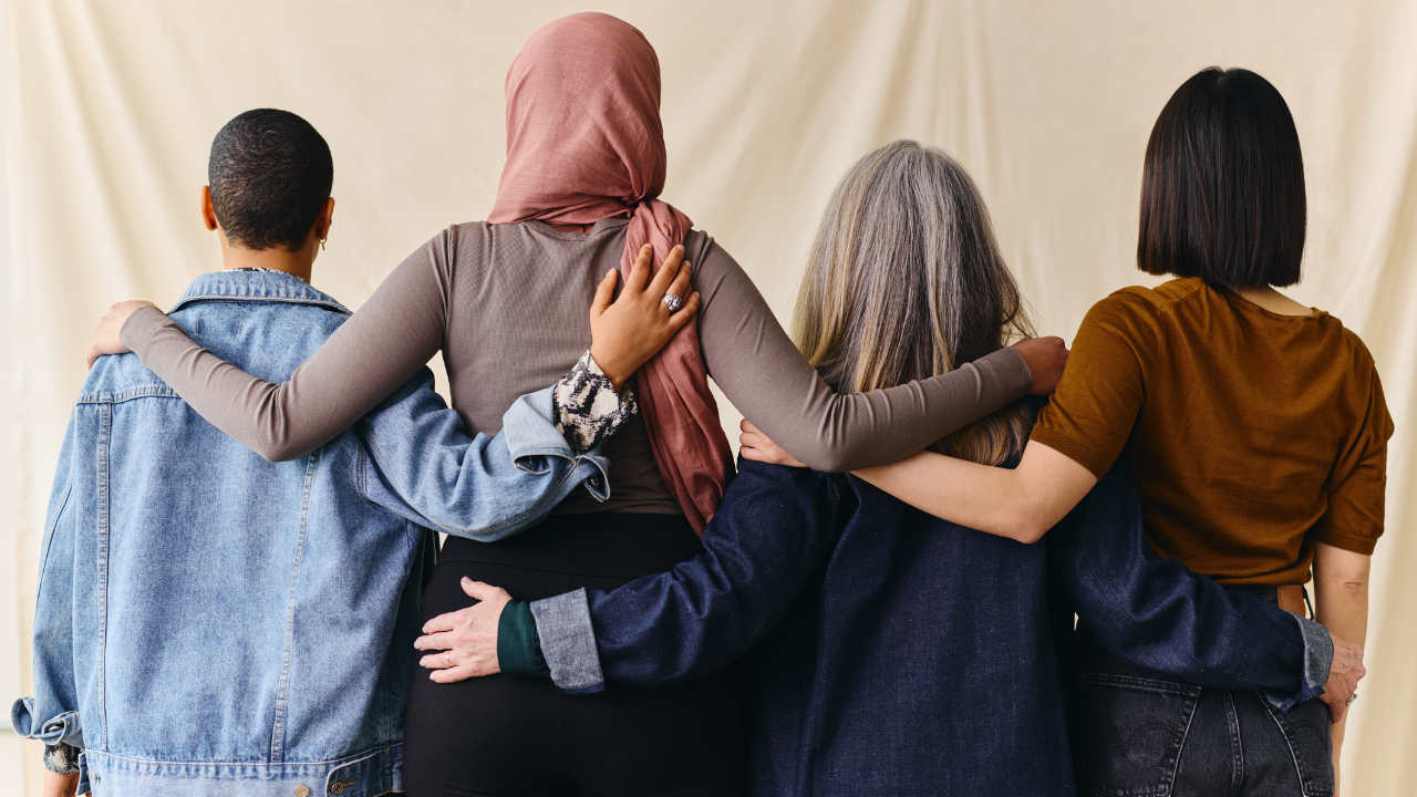 Photo of a group of women with their backs to the camera with their arms around eachother