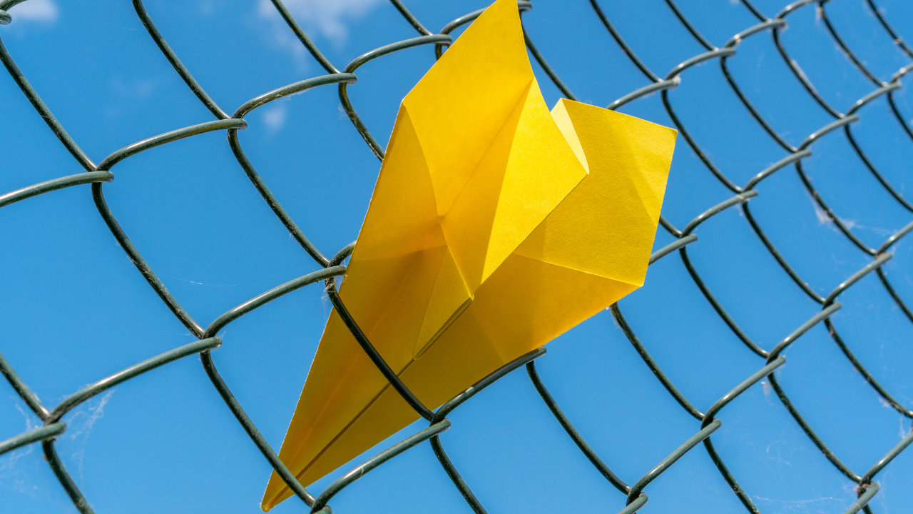 Photo of a paper aeroplane caught in a metal fence